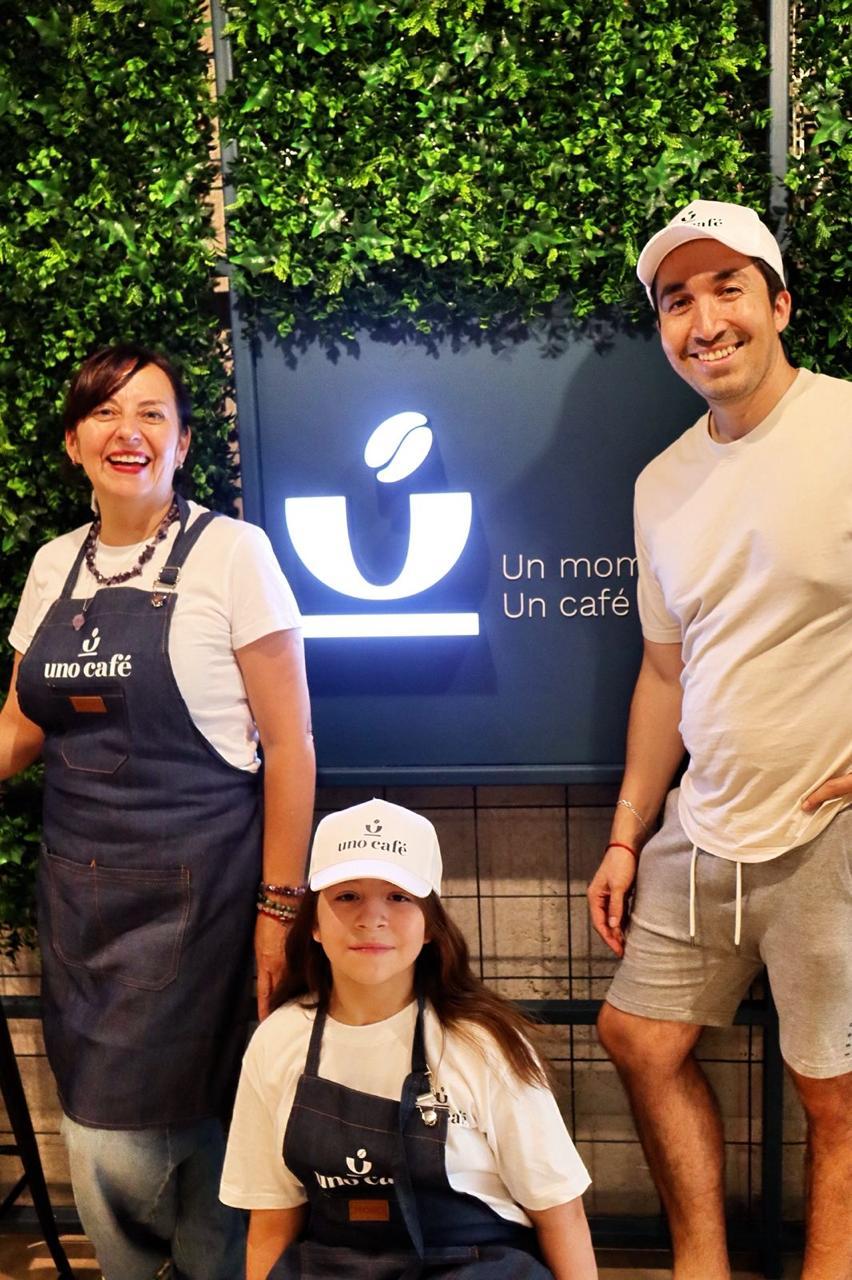 Equipo de Uno Café sonriendo frente al letrero iluminado del local